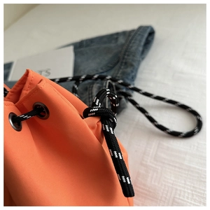 Close-up of vibrant orange nylon bucket bag with textured fabric and woven drawstring