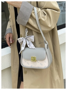 Fashionable crossbody bag with bow prints and metal clasp shown on beige trench coat