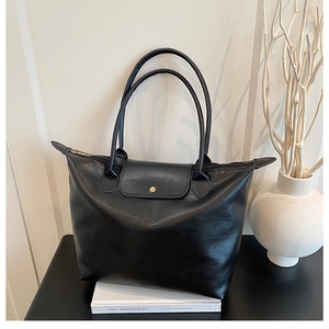 Detail of black tote bag featuring textured leather, gold snap button and long handles