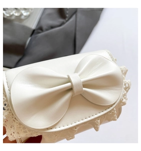 Detailed close-up of white leather handbag featuring a large bow and lace trim detail