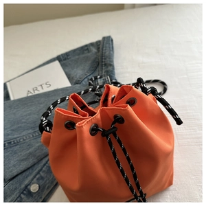 Detail of bright orange nylon bucket bag with bicolor drawstring and metal hardware