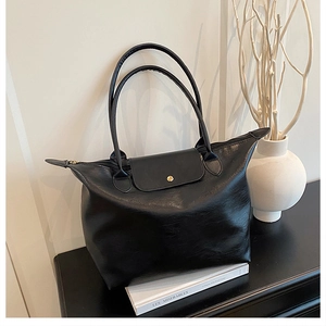 Detail of a black tote bag with top zipper and golden buckle flap for daily commuting