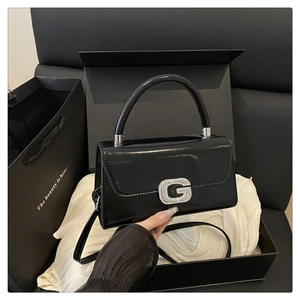 Close-up of glossy black handbag with rhinestone G buckle and elegant gift packaging