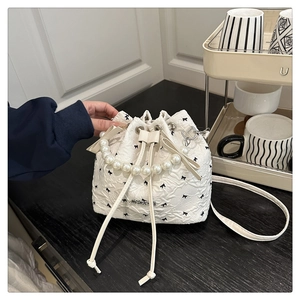 Détail du sac seau matelassé avec imprimés nœuds noirs et poignée en perles