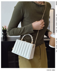 Detail of white pleated handbag with gold chain strap and woven handle on a model