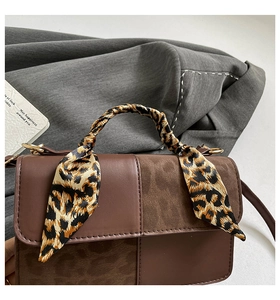 Detail of a brown shoulder bag with mixed leather textures and leopard print silk scarf handle