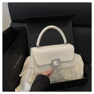 Detail of white glossy leather handbag with a sparkling diamond-encrusted G-buckle