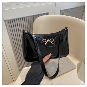 Detailed view of glossy black patent leather shoulder bag with gold bow clasp accent