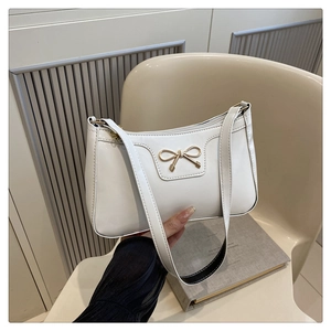 Detail of white leather shoulder bag featuring a decorative golden bow and sleek strap