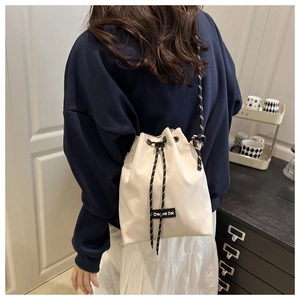 Detail of a beige drawstring bucket bag featuring a Creative Cat label and striped cords