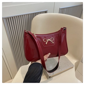 Detail of dark red patent leather underarm bag with gold bow metal hardware
