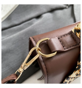 Detail of brown leather handbag with gold metal hook and leopard print silk scarf