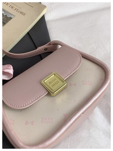Detail of pink bow handbag with metallic clasp and adjustable strap in a lifestyle setting