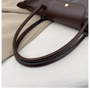 Detail of dark brown leather tote featuring a round gold metallic snap button closure