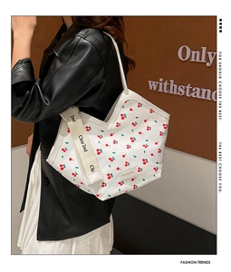 Detail of white tote bag featuring red cherry prints and stylish woven shoulder strap
