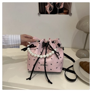 Détail d'un sac seau plissé rose avec poignée en perles et nœuds décoratifs noirs