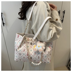 Detail of white pleated tote bag featuring pink floral prints and cute plush bear charm