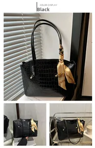 Détail d'un sac cabas noir motif crocodile avec une poignée décorée d'un foulard en soie
