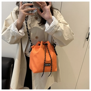 Detail of vibrant orange drawstring bucket bag with black and white woven rope strap