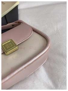 Close-up of golden square metal clasp and pink leather texture on a bow handbag