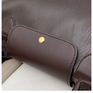 Close-up of deep brown pebbled leather texture and golden round snap button on tote bag
