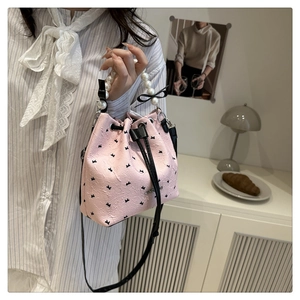 Sac seau rose avec motifs nœuds, poignée en perles et bandoulière porté par un mannequin