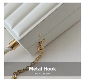 Close-up of golden metal hooks and chain on a white wave-textured crossbody handbag