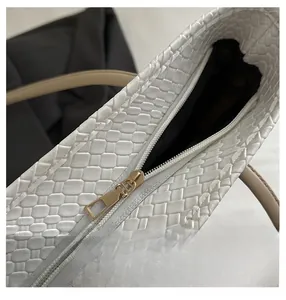 Close-up of smooth gold zipper on white woven tote bag with brown leather strap