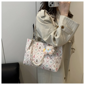 Detail of cream tote bag featuring textured fabric with bear prints and pearl chain strap