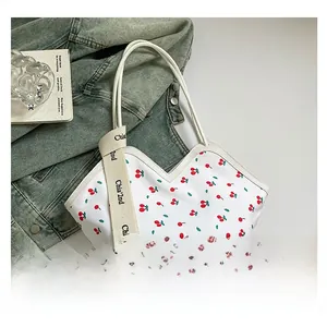 Detail of white tote bag with cherry print and wide branded crossbody strap on denim