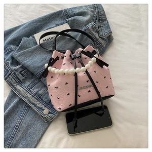 Detail of pink drawstring bucket bag featuring a textured bird print and pearl chain strap