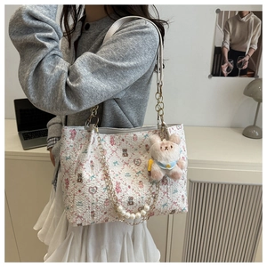 Close-up of floral tote bag with teddy bear print, pearl chain and plush charm