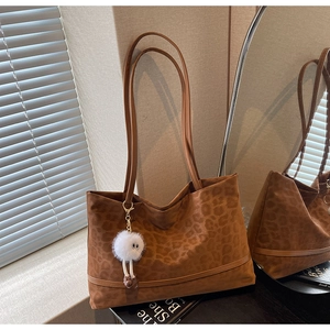 Detail of large brown leopard print tote bag with plush monster charm in soft natural light