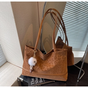 Detail of brown leopard print tote bag with white faux fur pompom charm and leather strap