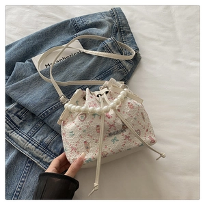 Detail of white floral bucket bag featuring pearl handle and embossed strawberry texture