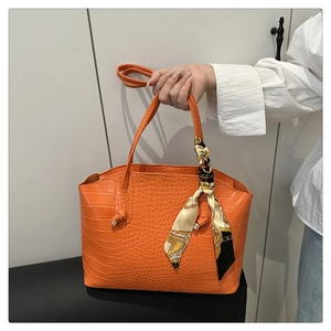 Gros plan d'un sac cabas orange à motif crocodile orné d'un foulard en soie imprimé