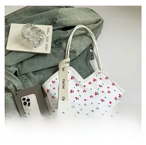 Detailed shot of white tote bag featuring red cherry prints and woven shoulder straps