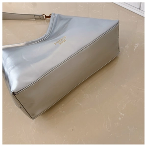 Détail d'un sac sous le bras argenté brillant avec lettrage doré et structure trapézoïdale