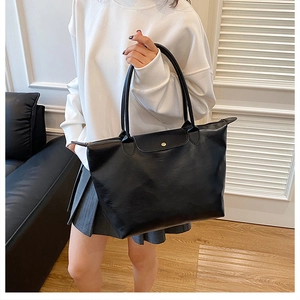 Detail of black leather tote bag with gold buckle and top handle shown on a model
