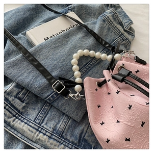 Detailed view of pink pleated bucket bag with rabbit print and faux pearl handle on denim