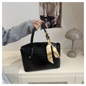 Détail du cabas noir à motif crocodile avec une écharpe décorative en soie sur la poignée