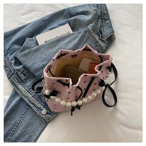 Pink bucket bag with pearl handle and black bow detail shown in a lifestyle setting