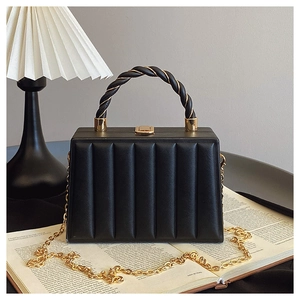 Close-up of black pleated tote bag with twist handle and gold chain on open book