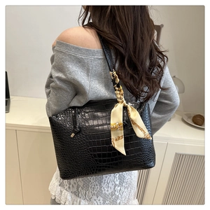 Dettaglio della borsa tote nera con motivo a coccodrillo e foulard decorativo in seta