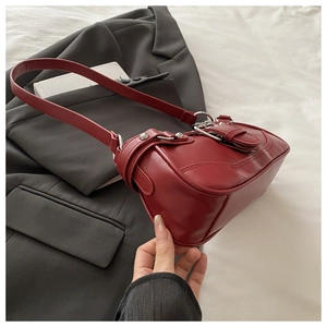 Close-up of deep red vintage shoulder bag with silver studs on a grey suit background