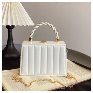 Macro detail of white pleated leather handbag with gold chain on a book