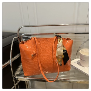 Détail d'un sac cabas orange à motif crocodile avec foulard décoratif sur la poignée