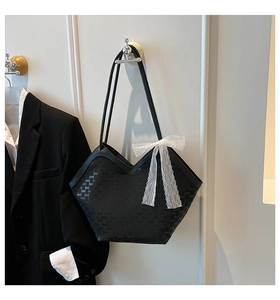 Détail du sac seau noir avec motif à logo et décoration de nœud en dentelle blanche