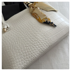 Gros plan du sac cabas blanc à motif crocodile avec foulard en soie jaune sur l'anse