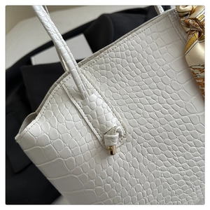 Gros plan d'un sac à main blanc à motif crocodile avec poignée nouée et foulard en soie